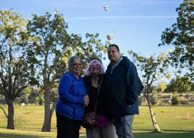 Three golf tournament participants standing next to a course with hot air balloons floating through the sky.