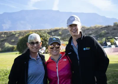 Three golf tournament participants standing on the golf course with golf cart in background.
