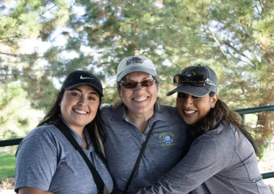 Three golf tournament participants standing on the golf course next to a pine trees.