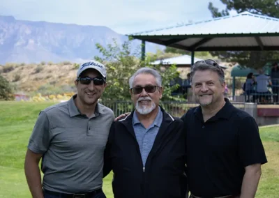 Three golf tournament participants standing on the golf course next to a shade structure.